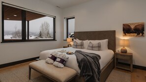 A bedroom with a large bed, a bench, a nightstand, a lamp, and a painting.