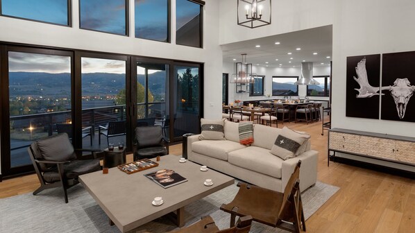 A spacious living area with a large window overlooking a scenic view, a cozy seating arrangement, and a modern kitchen in the background.