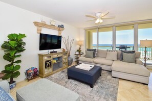 A living room with a flat-screen TV, a sofa, a coffee table, and a large window with a view of the ocean.