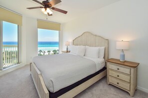 Ein Schlafzimmer mit einem großen Bett, zwei Nachttischen, einem Deckenventilator und Blick auf den Strand.