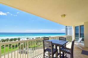 Ein Balkon mit Blick auf den Ozean und den Strand, inklusive Tisch, Stühlen und Geländer.