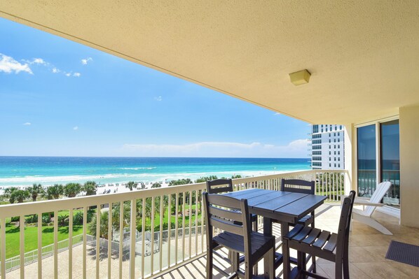 A balcony with a view of the ocean and beach, a table, chairs, and a railing.