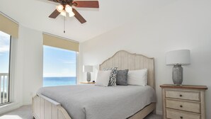 A bedroom with a large bed, a nightstand, a ceiling fan, and a view of the ocean. - 5th Floor 3 Bedroom Condo with Semi-Private Elevator (Destin)