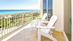 A balcony with two white Adirondack chairs, a glass door, and a view of the ocean and greenery. - 5th Floor 3 Bedroom Condo with Semi-Private Elevator (Destin)