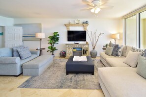 A living room with a sofa, a coffee table, a TV, and a ceiling fan. - 5th Floor 3 Bedroom Condo with Semi-Private Elevator (Destin)