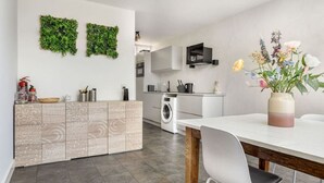 Une cuisine moderne dotée d’un lave-linge encastré, d’un coin repas avec une table et des chaises blanches, et de panneaux muraux verts décoratifs.