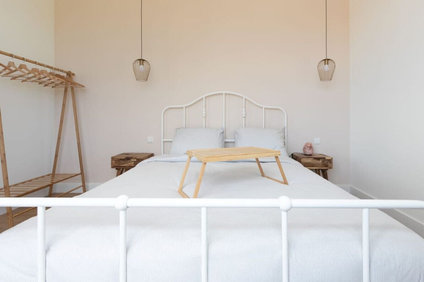 Une chambre à coucher comprenant un lit, des tables de chevet en bois, un étendoir en bois et deux lampes suspendues.