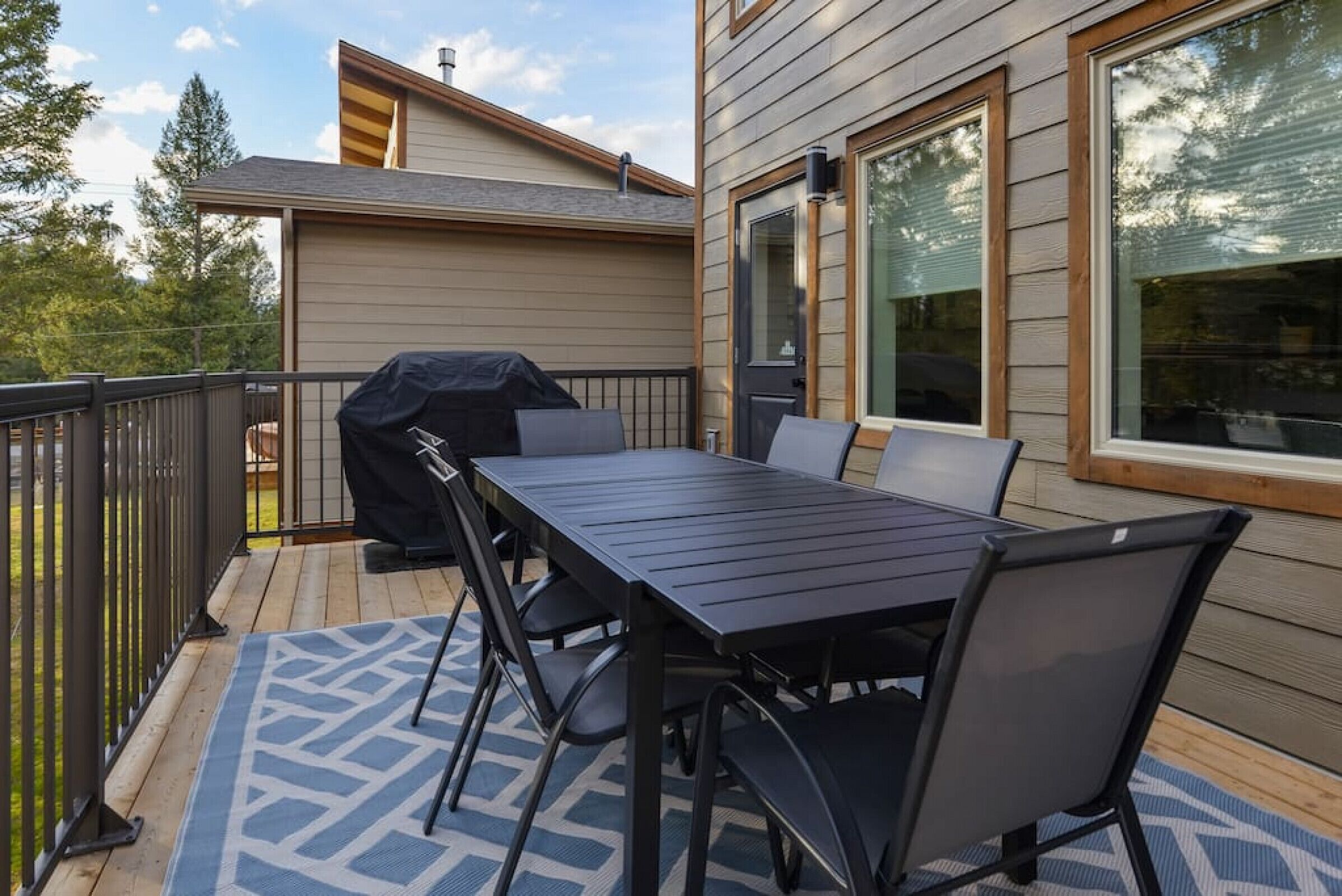 Une terrasse extérieure avec une table et des chaises, un barbecue et une vue sur une maison dotée de grandes fenêtres.