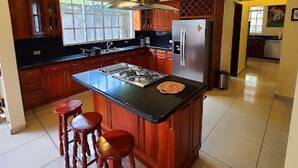 Una cucina con isola centrale, sgabelli da bar in legno, frigorifero in acciaio inossidabile e pensili in legno.