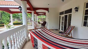 A covered porch with a hammock, a chair, and a view of greenery.