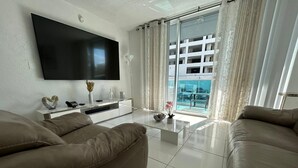 A modern living room with a flat-screen TV mounted on the wall, a glass coffee table, two leather sofas, and a large window with curtains. - Hollywood beach apartment on the beach the biggest in the building all new  (Hollywood)