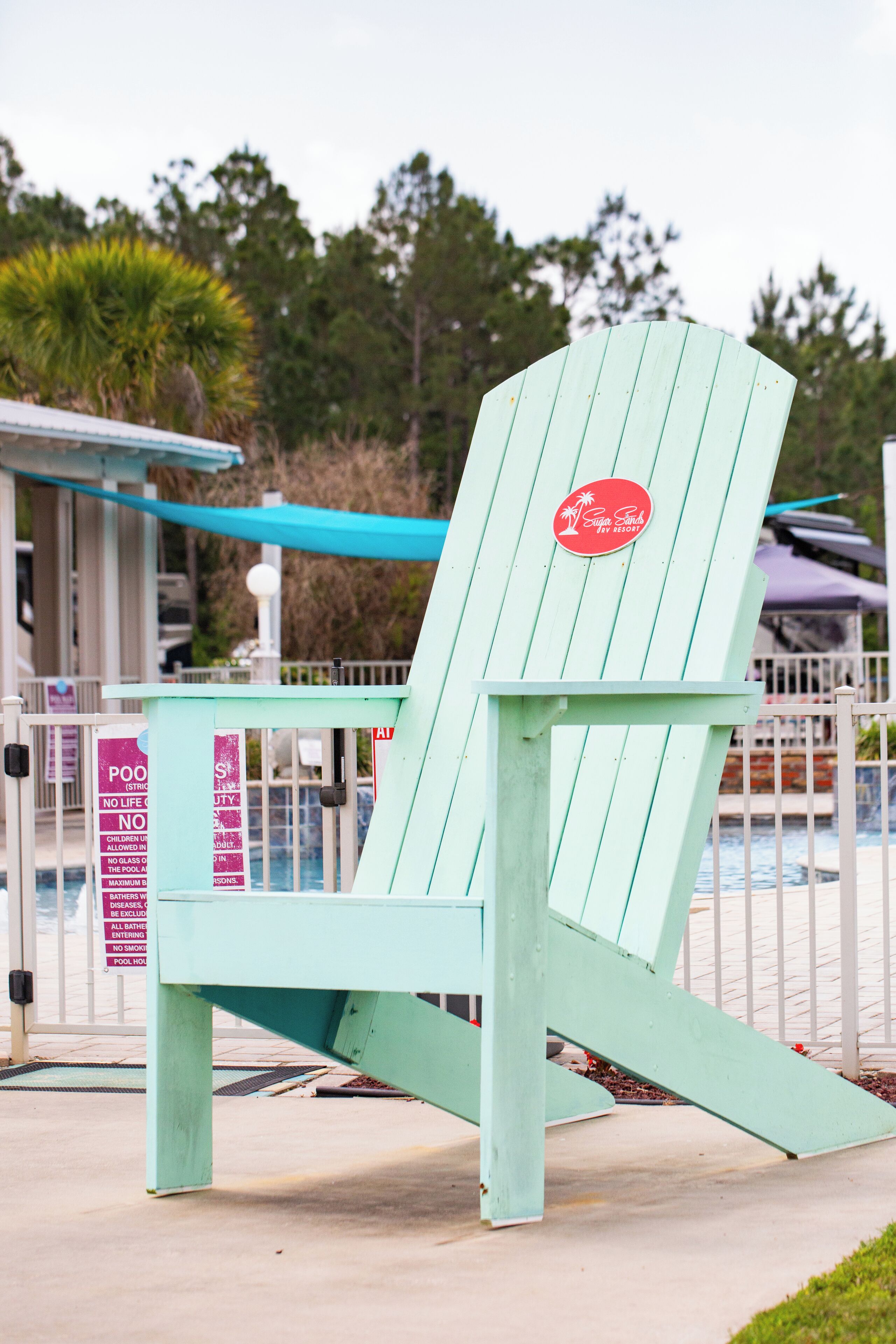 A light blue Adirondack chair with a red logo, positioned outdoors near a pool area.