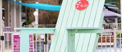 A light blue Adirondack chair with a red logo, positioned outdoors near a pool area.