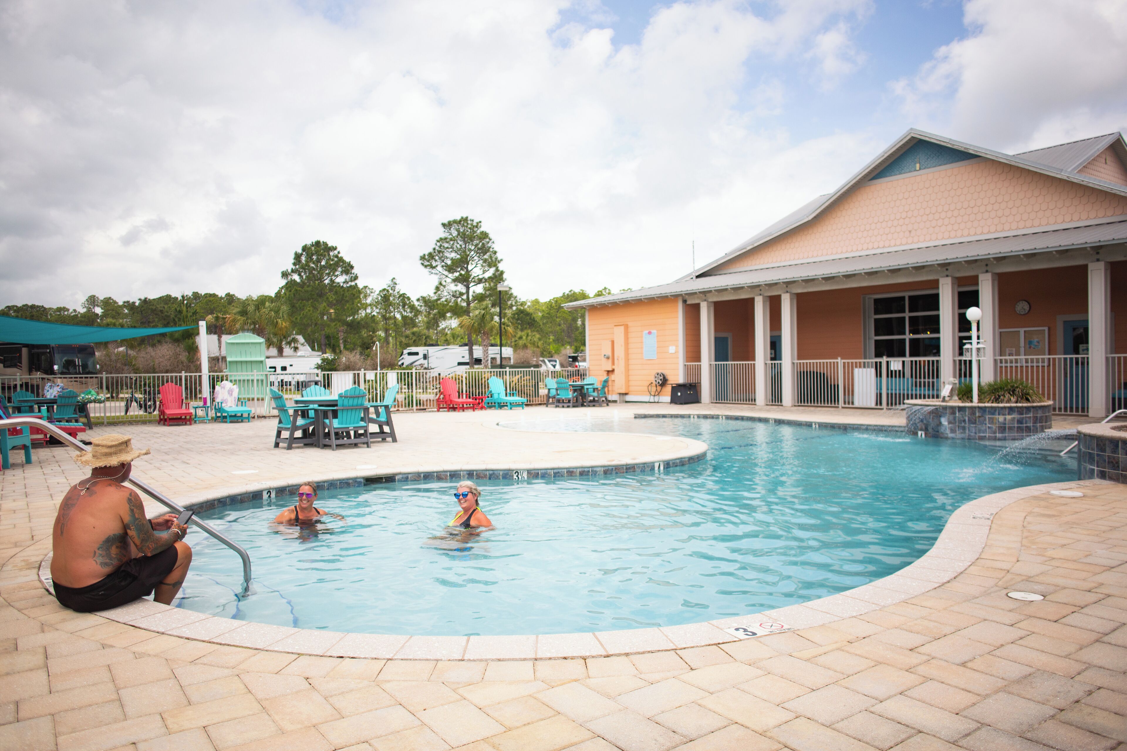 A swimming pool area with a covered seating area, a building with a tiled roof, and a fenced outdoor space.