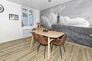 A dining area with a large table and chairs, a view of the sea through a window, and a mural of a lighthouse. - Gîte bord de mer "A l'abordage" Exceptional view (Fécamp)