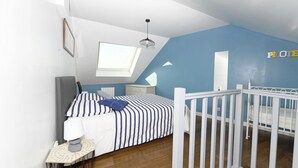 A bedroom with a bed, a nightstand, a desk, a crib, a window, and a ceiling light. - Gîte bord de mer "A l'abordage" Exceptional view (Fécamp)