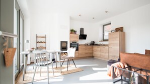 Une cuisine moderne avec des meubles blancs, un coin repas avec une table et des chaises, et un espace salon confortable avec un canapé et une cage pour animaux de compagnie.