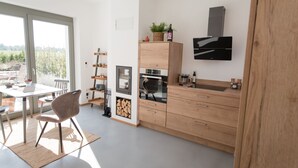 Une cuisine moderne avec des meubles en bois, un four encastré et une grande fenêtre donnant sur un jardin.