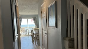 A hallway with a wooden floor, a staircase, and a door leading to a balcony with a view of the ocean. - Beach Front Property with Stunning  Ocean Front View in the Ocean Dunes Resort (Kure Beach)