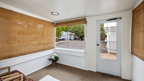 A room with a large window, a door, a bench, and a small table with a vase of flowers. - Charming Home in Prescotts Historic District. Less than a mile from Whiskey Row. (Prescott)