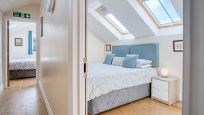 A bedroom with a skylight, a bed with blue bedding, a bedside table with a lamp, and a framed picture on the wall.