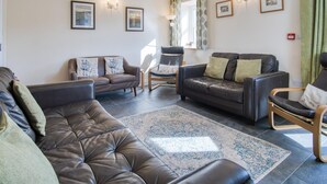 A living room with a brown leather sofa, a black leather couch, and a wooden chair. There are framed pictures on the wall and a window with curtains.