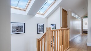 A hallway with skylights, wooden railings, and framed pictures on the walls.