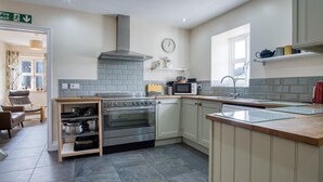 A modern kitchen with a built-in oven, microwave, and sink. There is a clock on the wall and a fire exit sign above the door.