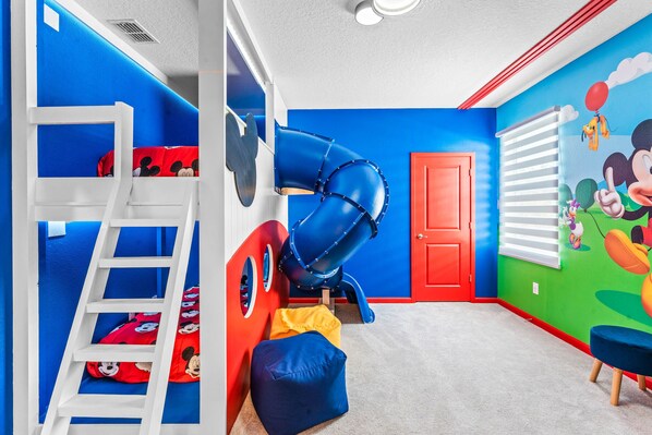 Une salle de jeux pour enfants avec un toboggan, des lits superposés et des décorations murales colorées.