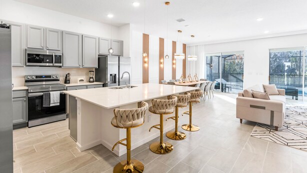 Una cocina moderna con una isla central, taburetes de bar y un comedor con sofá y sillas.