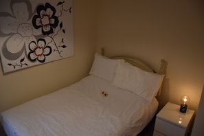 A neatly made bed with white bedding and a single pillow, a bedside table with a lamp, and a wall-mounted floral artwork. - Scandinavian City Centre Apartment (Worcester)