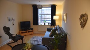 A living room with a sofa, a TV, a dining table with chairs, and a potted plant. - Scandinavian City Centre Apartment (Worcester)