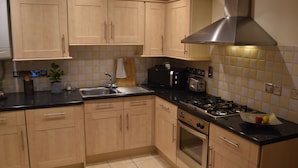 A kitchen with wooden cabinets, a black countertop, a stainless steel range hood, and a tiled backsplash. - Scandinavian City Centre Apartment (Worcester)
