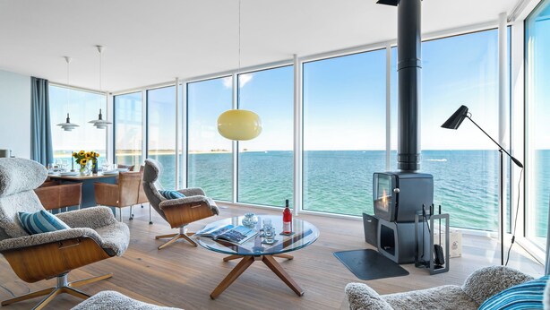 Una sala de estar moderna con un ventanal grande, una chimenea y un comedor con vista al mar.