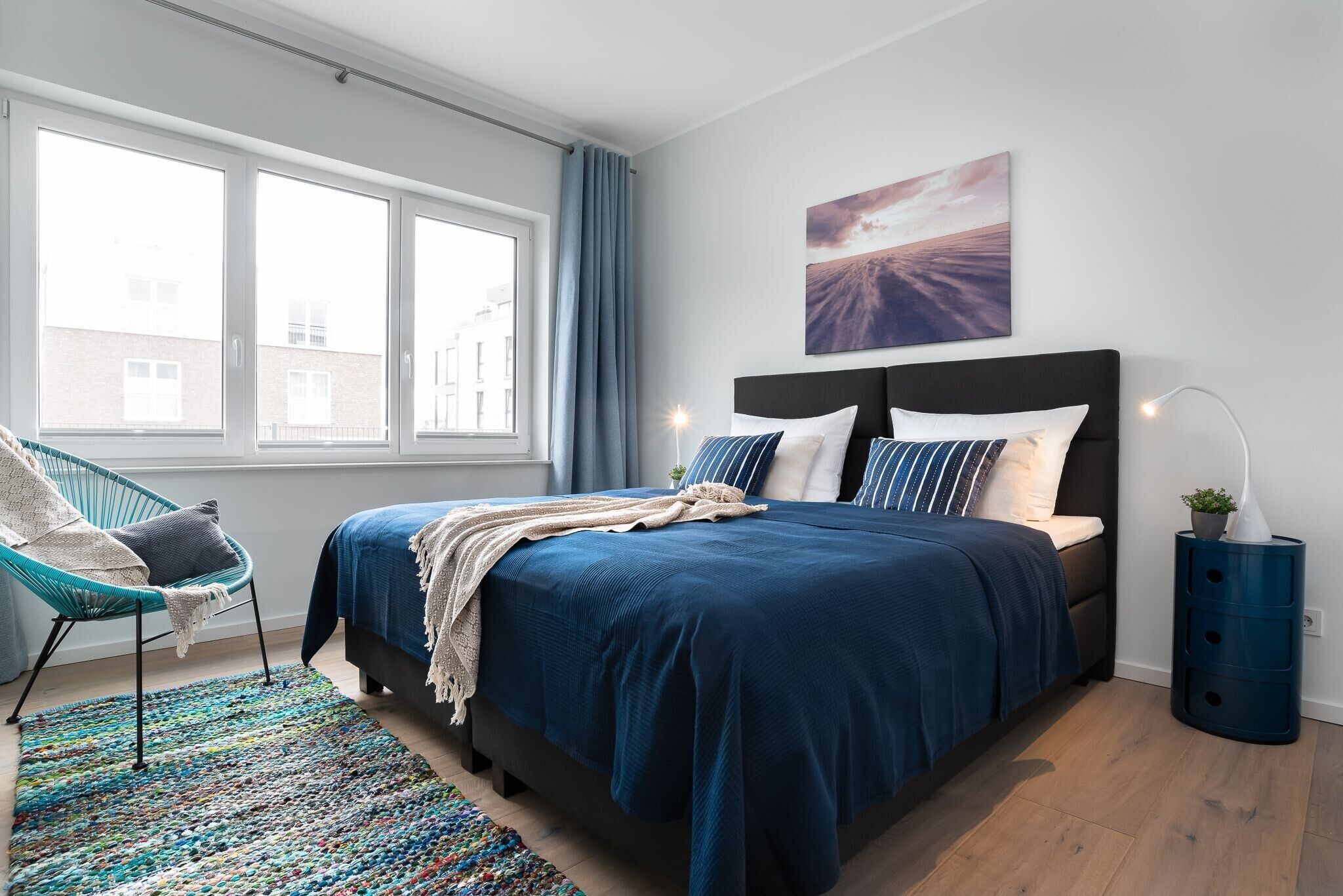 A modern bedroom with a large bed, a chair, a view of the city, and a painting on the wall.