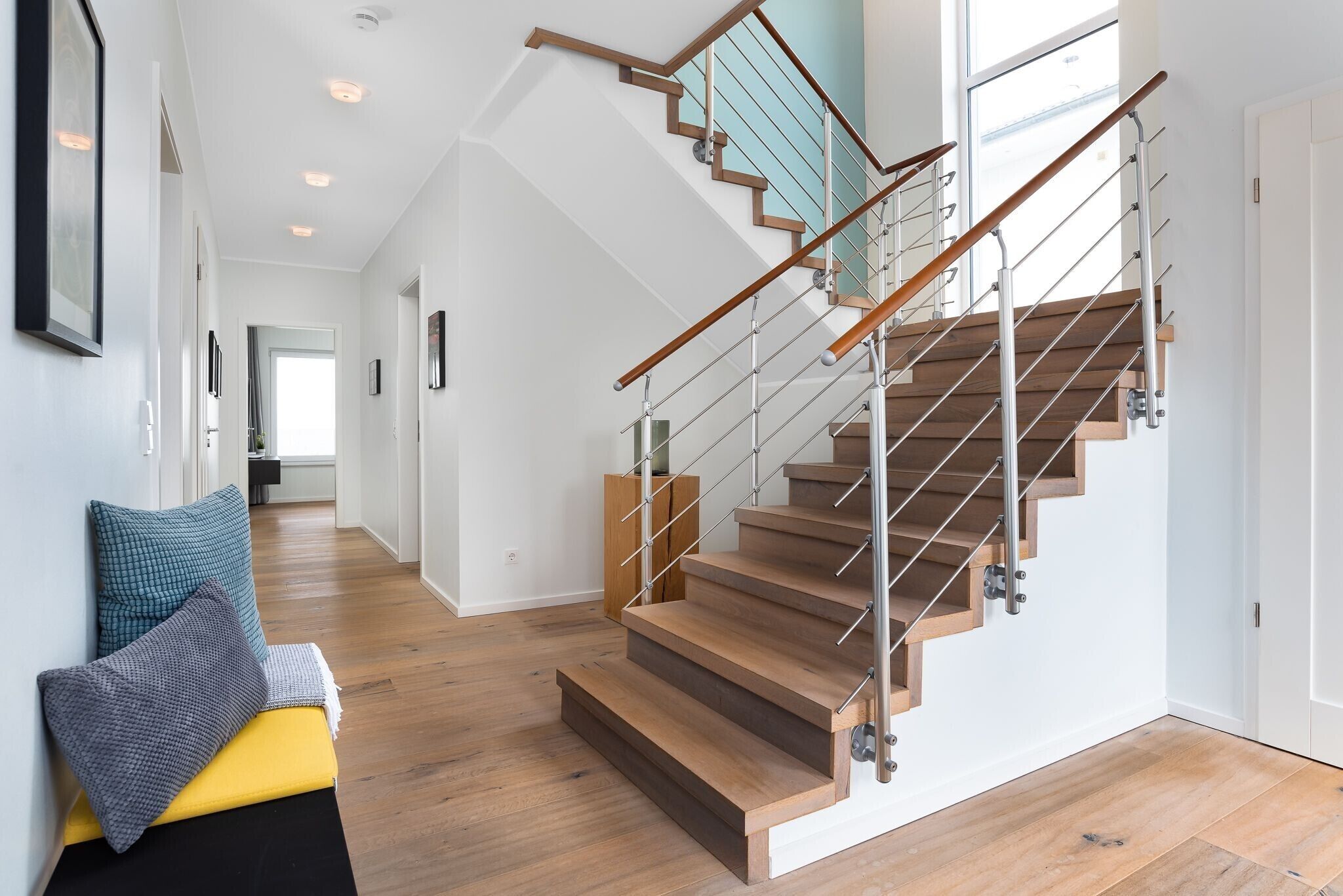 A modern staircase with wooden steps and metal railings, leading to a second floor.