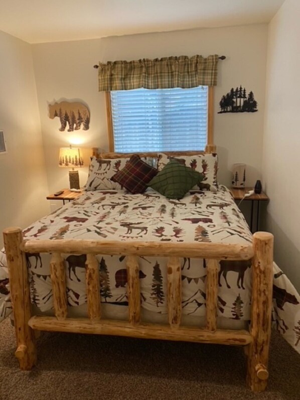 A bed with a forest-themed bedspread, a wooden headboard, and a window with blinds.