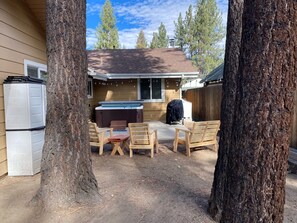 A backyard with a hot tub, wooden chairs, and a barbecue grill.
