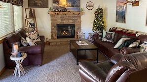 Un salon chaleureux avec une cheminée en pierre, des canapés en cuir, un sapin de Noël et des décorations de fêtes.