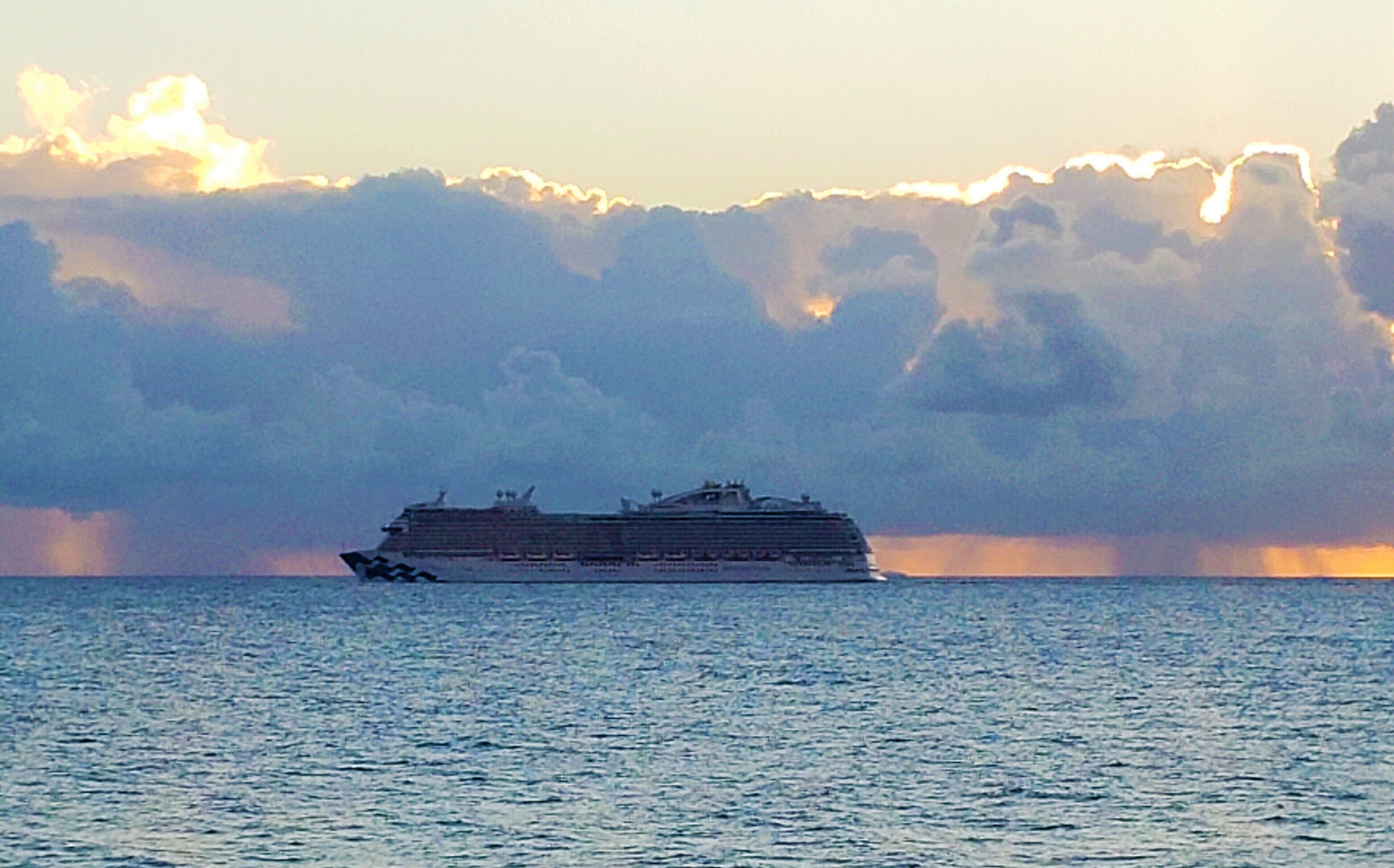 A cruise ship on calm waters with a sunset in the background.