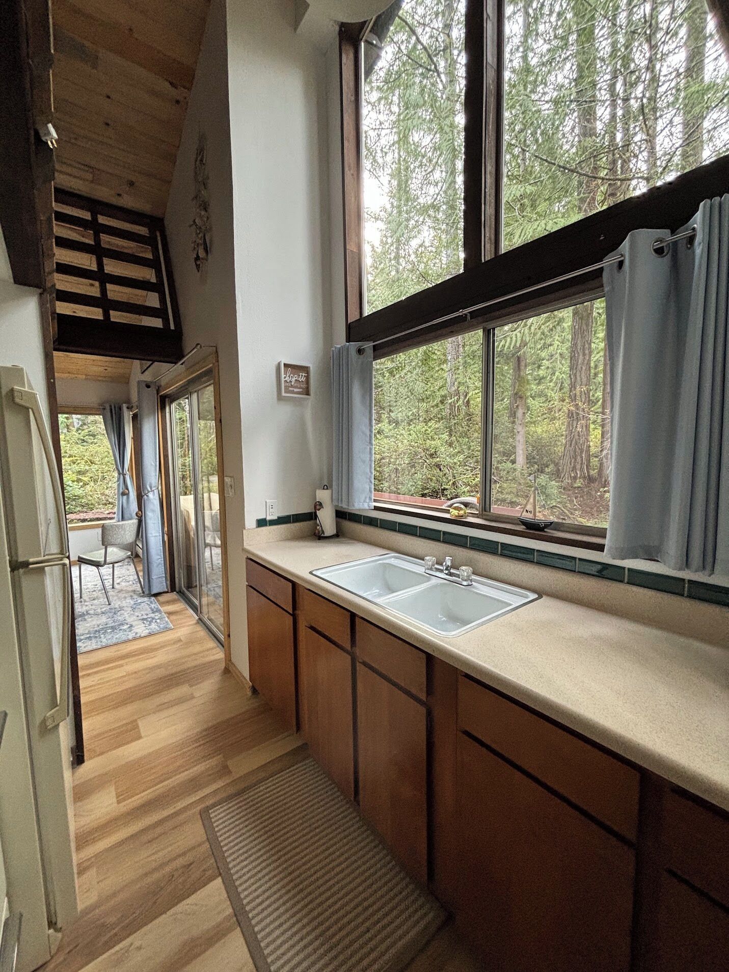 Una cocina con armarios de madera, un lavamanos doble y una ventana con vistas a árboles.