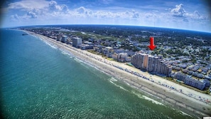Vue aérienne d’une ville côtière avec une longue plage, de hauts immeubles et un quartier résidentiel densément peuplé.