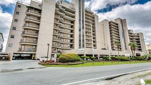 Un hôtel à plusieurs étages doté de balcons, d’un parking souterrain et d’un espace paysager agrémenté de petits arbres.