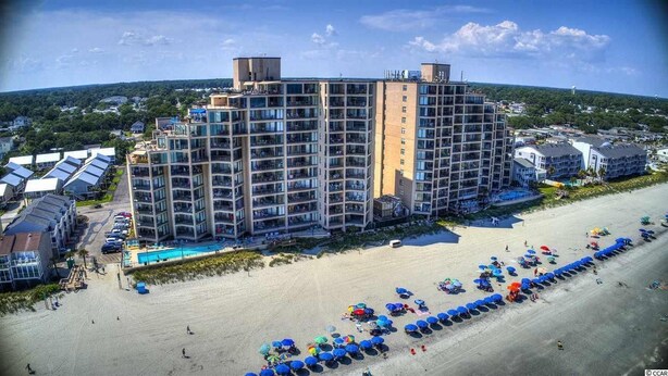 Un grand hôtel avec de nombreux étages, une piscine et un espace de plage équipé de parasols.
