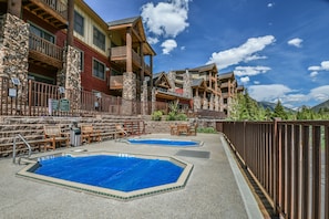 A pool area with two pools, wooden deck chairs, and a stone wall.