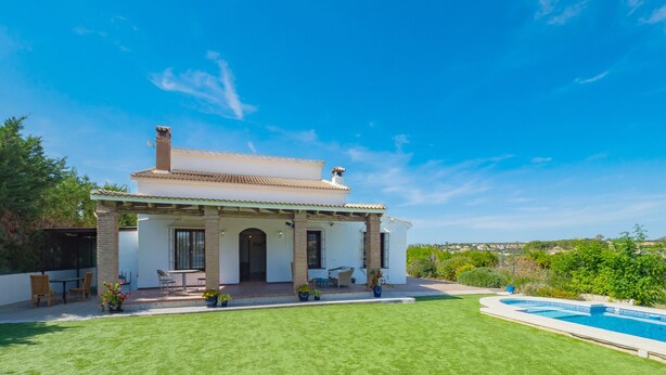 Una casa de dos pisos con piscina, un patio con mobiliario exterior y un césped bien cuidado.