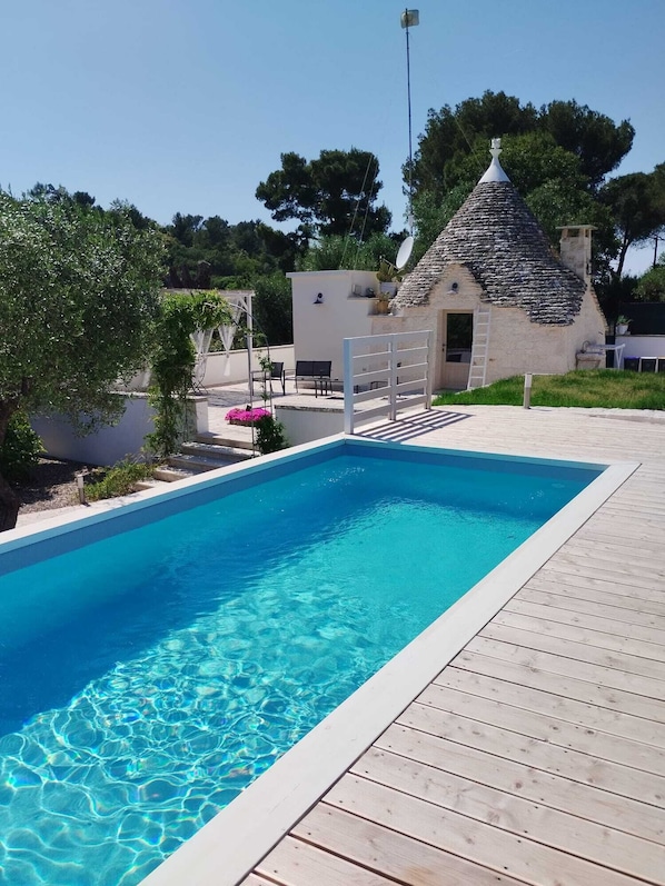 A swimming pool with a wooden deck, a stone building with a conical roof, and a satellite dish.