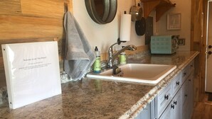 Une cuisine avec un plan de travail en granit, un évier, une serviette, un distributeur de liquide vaisselle et une casserole en métal accrochée au mur.
