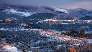 Une vue panoramique d’un paysage enneigé, avec une route sinueuse, des bâtiments et une chaîne de montagnes en arrière-plan.