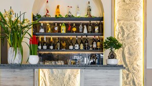 Una zona de bar con una pared de piedra, una estantería llena de botellas y tres taburetes.